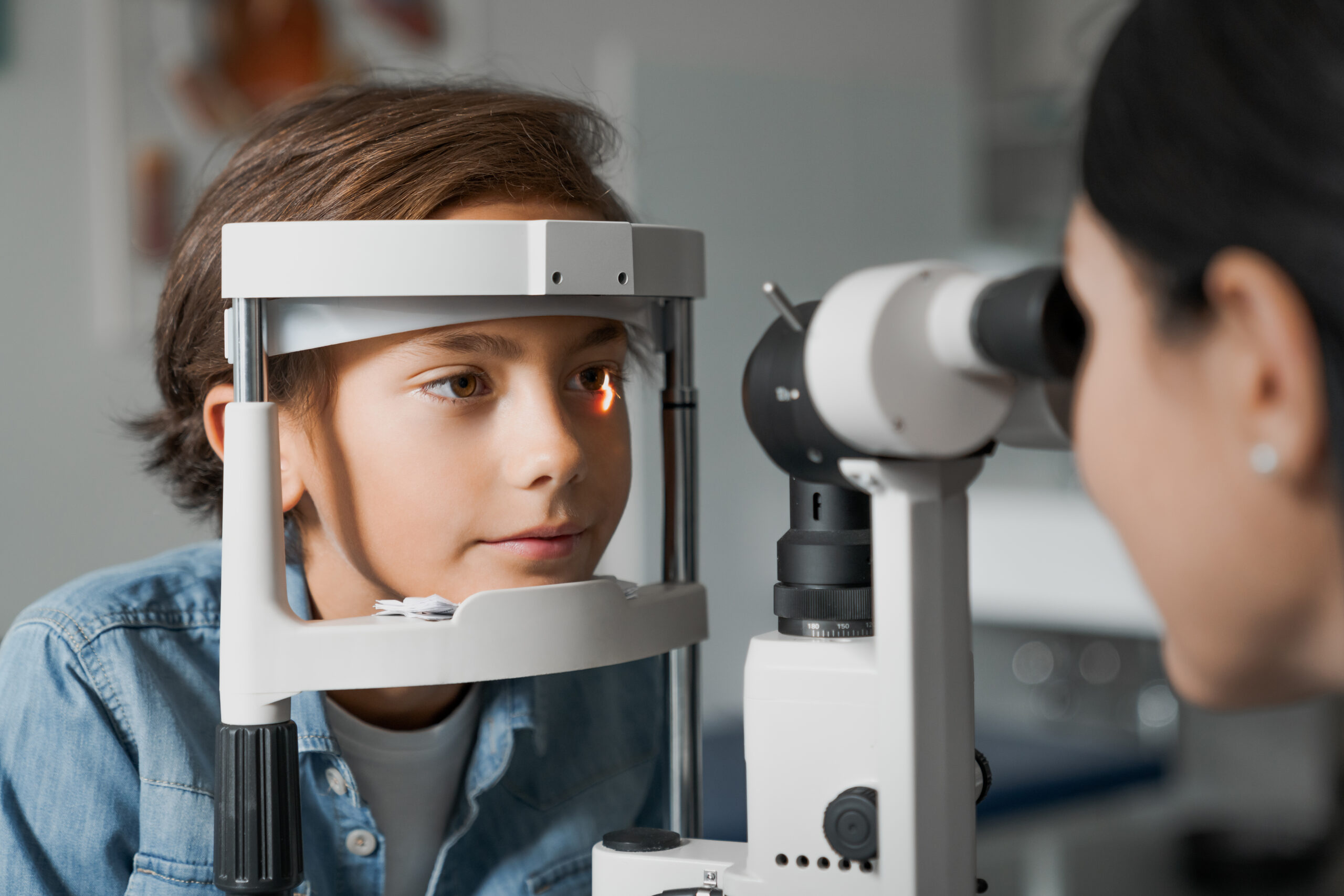 Adult female doctor ophthalmologist is checking the eye vision of cute child in modern clinic